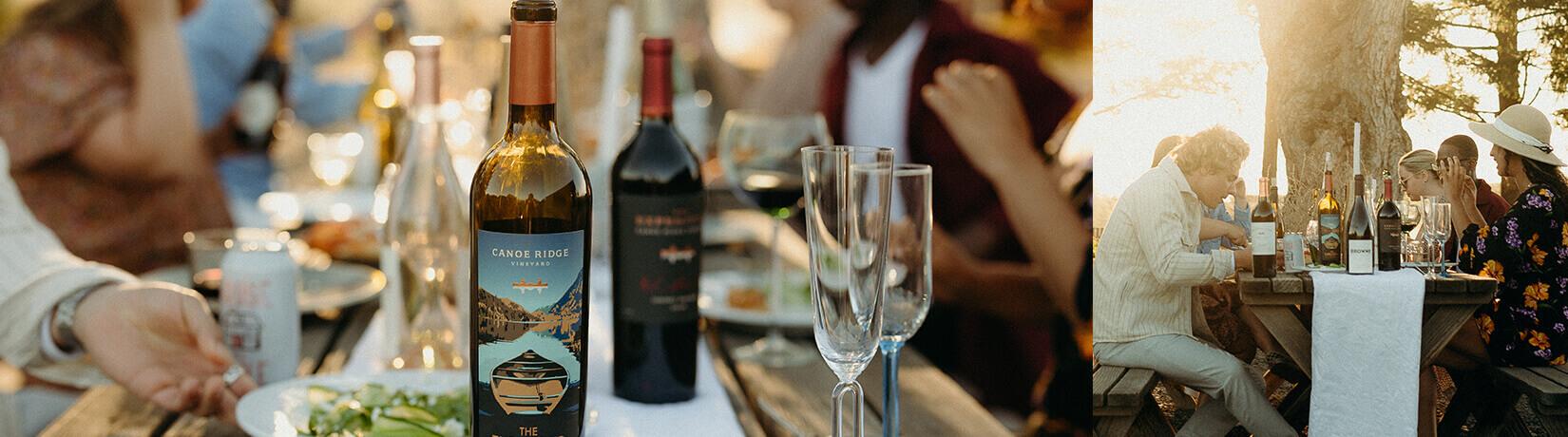 people enjoying wine and food around a picnic table at sunset