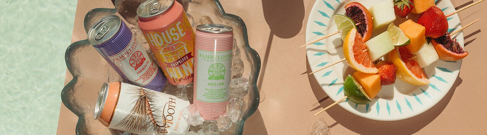 cans of wine coolers next to a plate of fruit kabobs